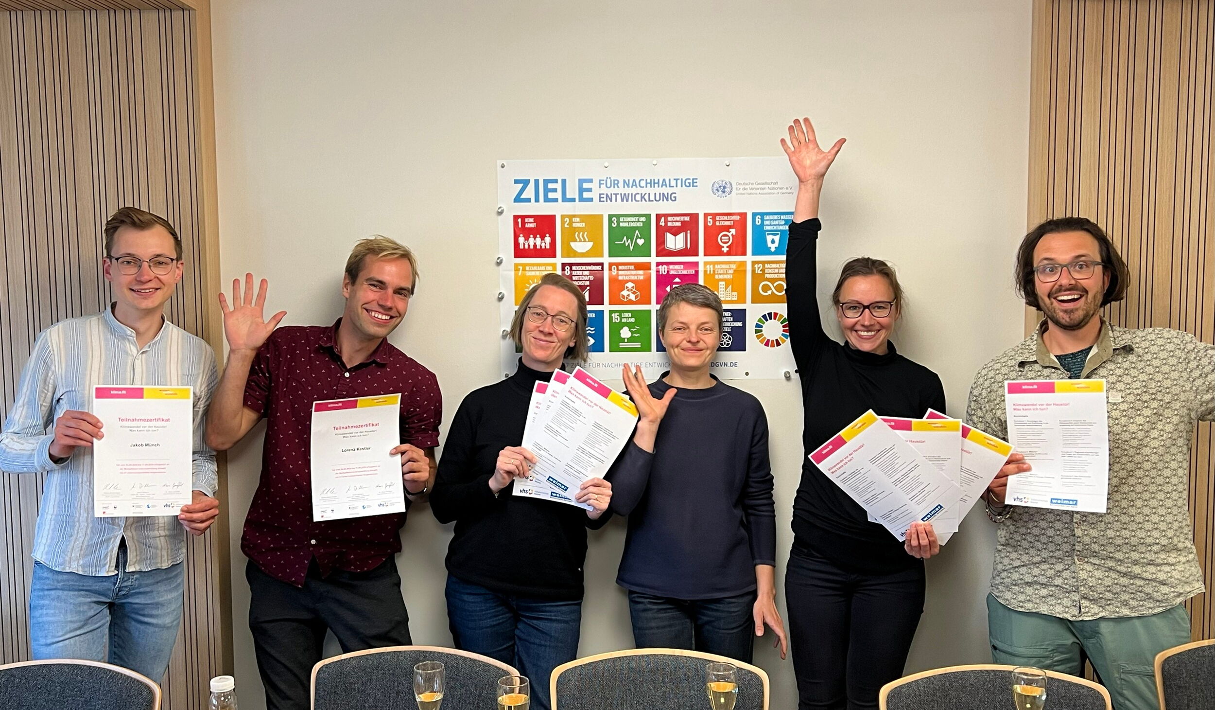 Teilnehmende eines Klimafit Kurses (6 Personen) stehen vor einem Plakat auf dem die Ziele für nachhaltige Entwicklung abgebildet sind.