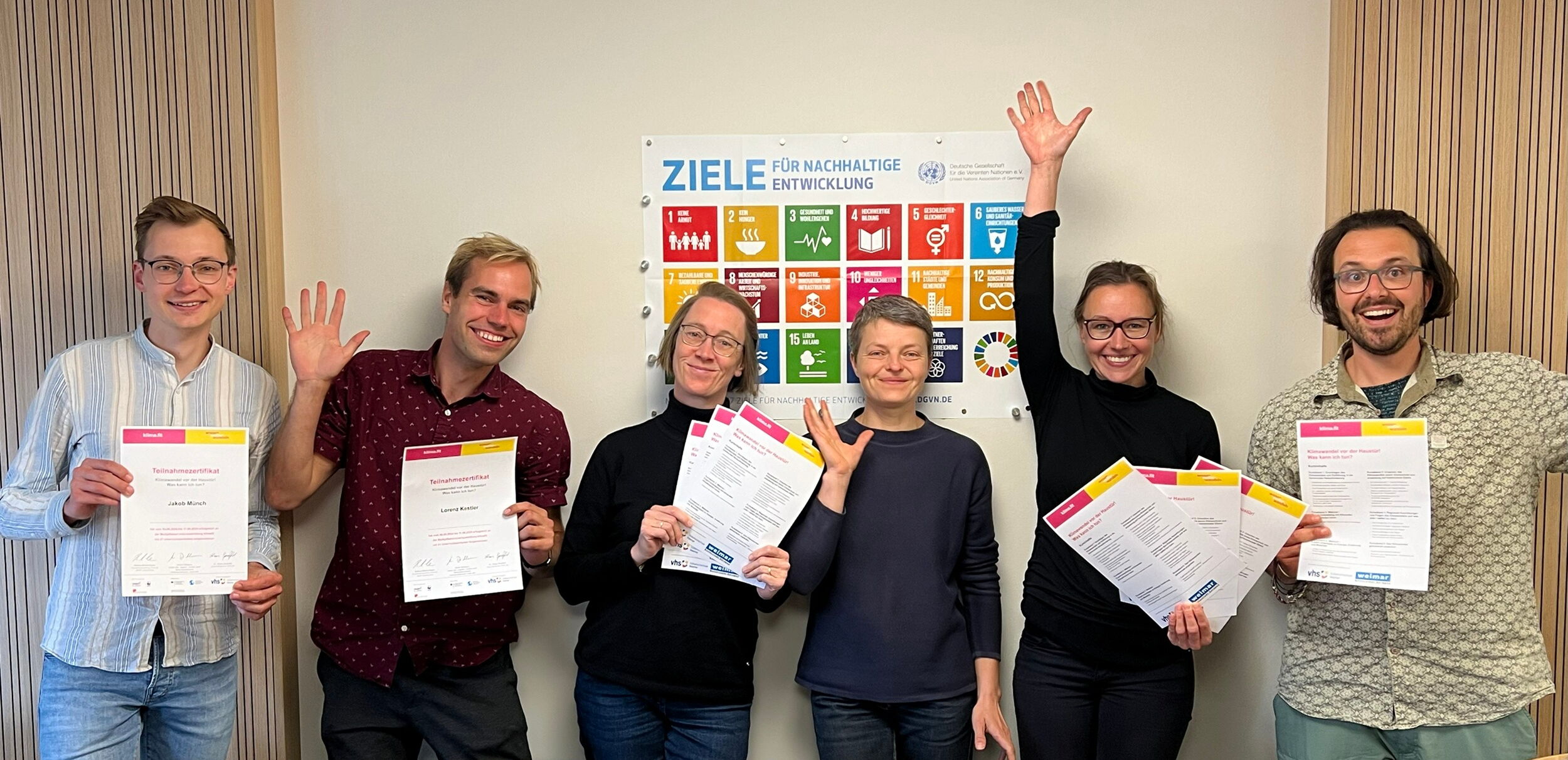 Teilnehmende eines Klimafit Kurses (6 Personen) stehen vor einem Plakat auf dem die Ziele für nachhaltige Entwicklung abgebildet sind.