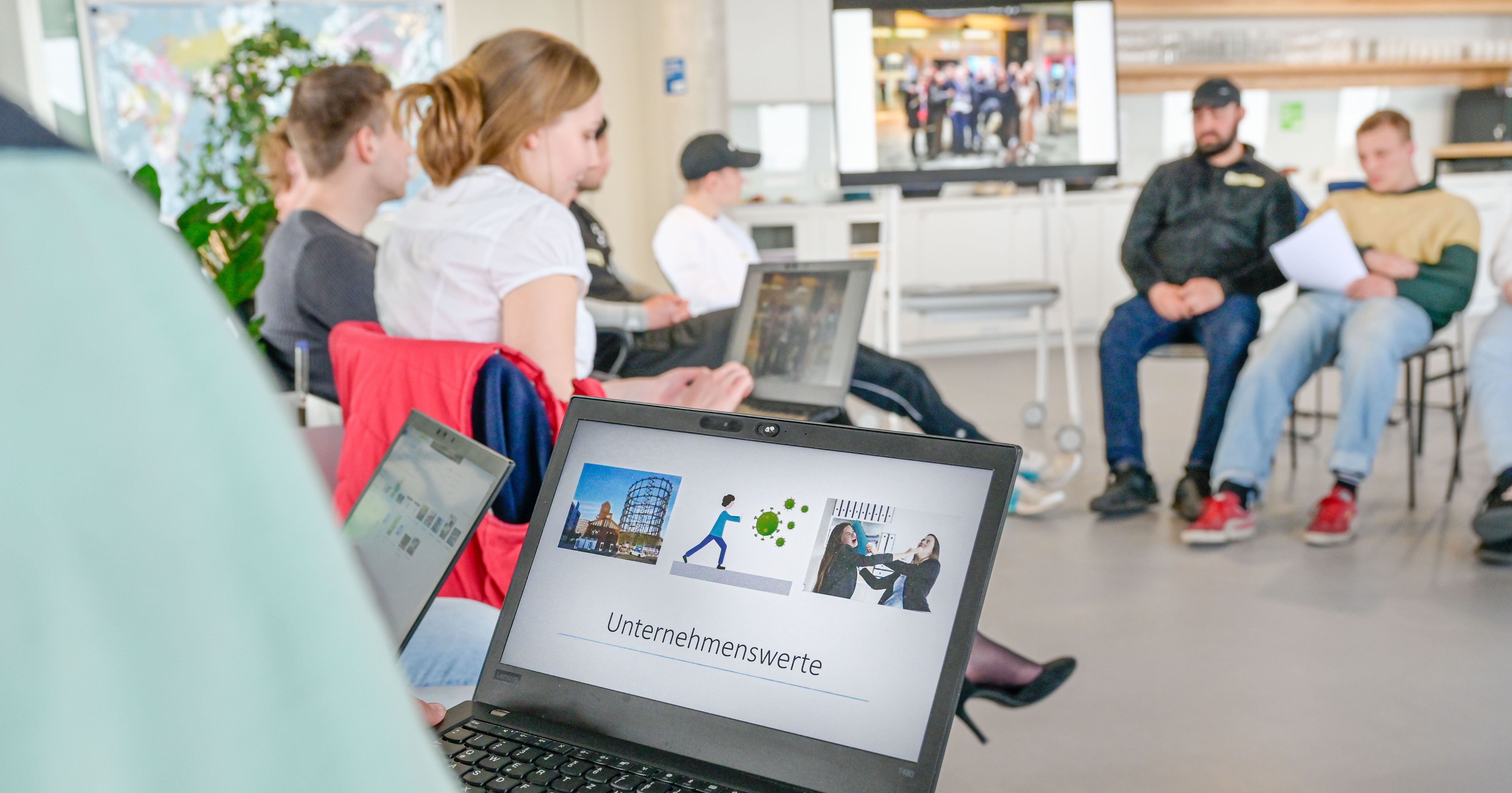 Personen sitzen im Kreis mit Laptops auf dem Schoß und besprechen sich