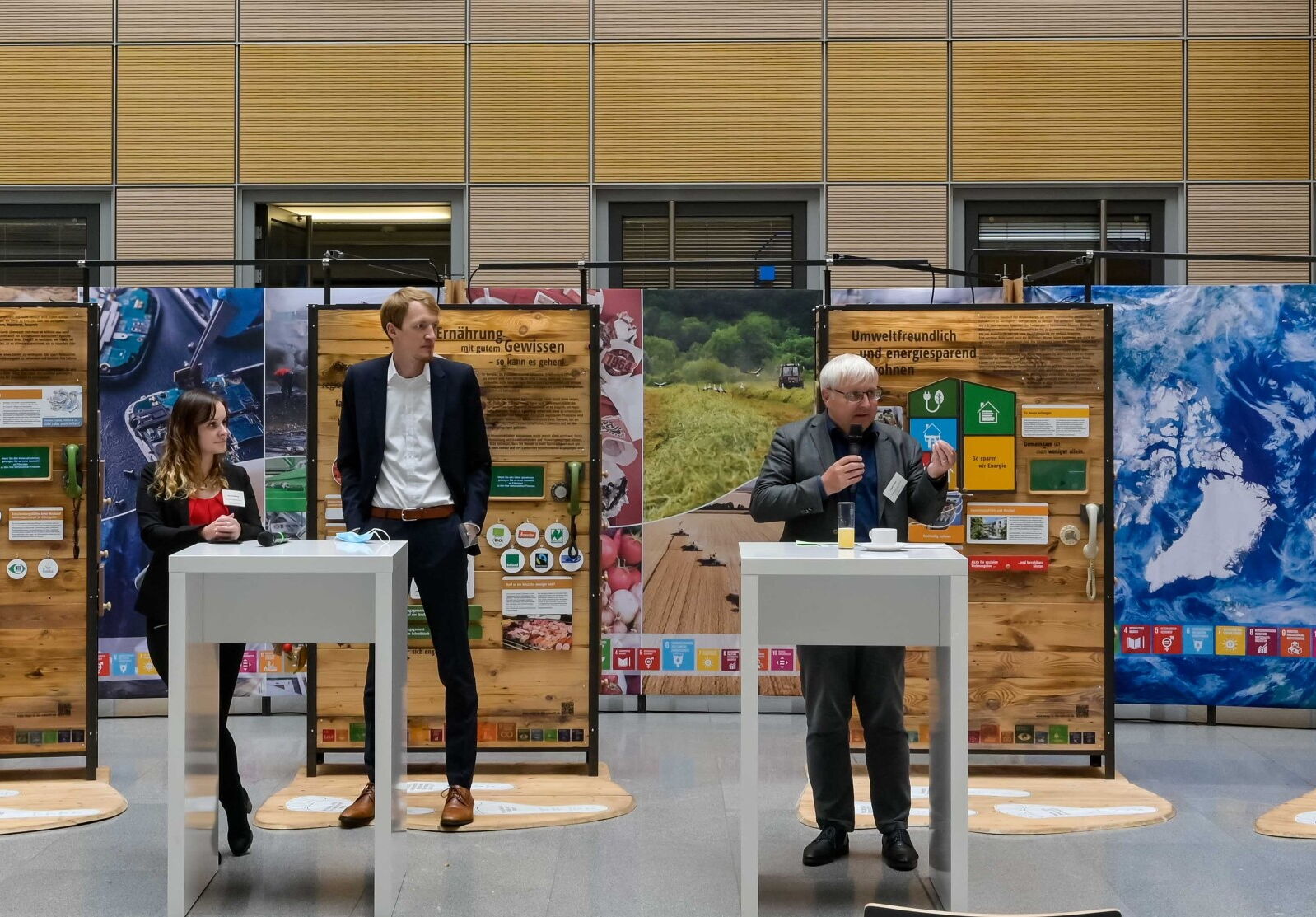 An vier Rednerpulten stehen insgesamt fünf Personen, die miteinander reden. Im Hintergrund sind Ausstellungsteile zu sehen.