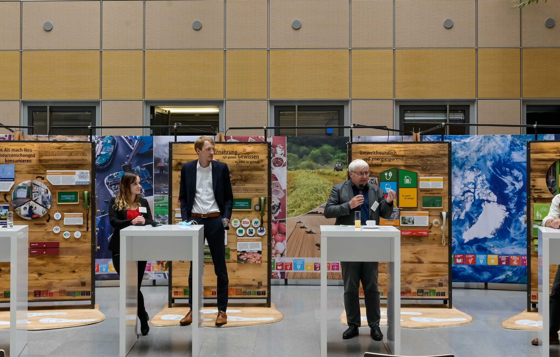 An vier Rednerpulten stehen insgesamt fünf Personen, die miteinander reden. Im Hintergrund sind Ausstellungsteile zu sehen.