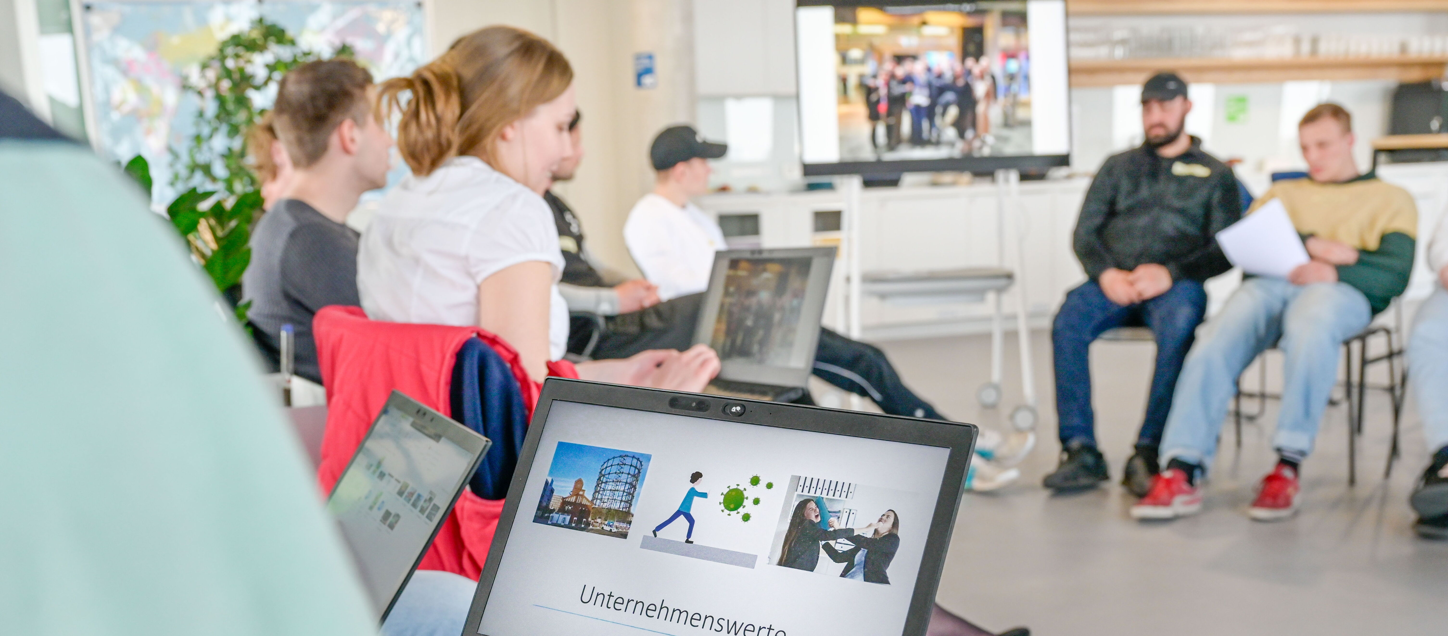Personen sitzen im Kreis mit Laptops auf dem Schoß und besprechen sich